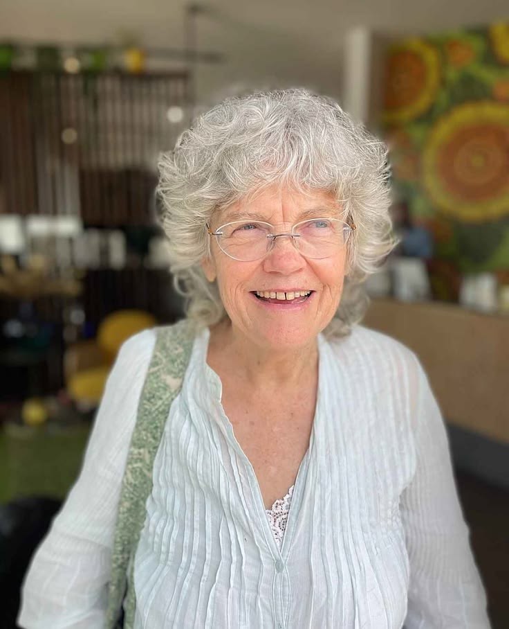 smiling woman over 70 with a curly gray bob wearing classic glasses