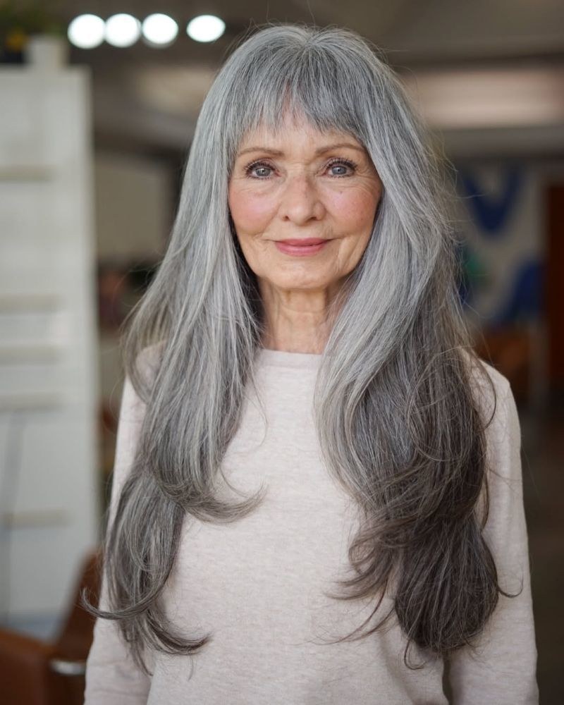 Woman over 70 with a long silver layers with a full fringe — hairstyle that helps a woman over 70 look fresh and younger