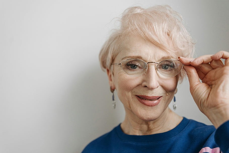 woman over 70 with pearl-white layered hair wearing delicate glasses