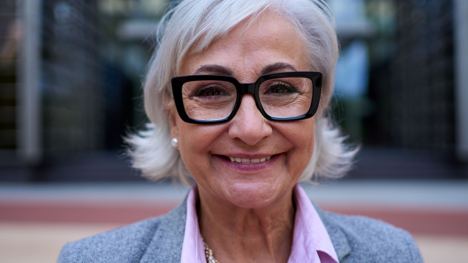 smiling woman over 70 with a feathered white bob wearing bold square glasses