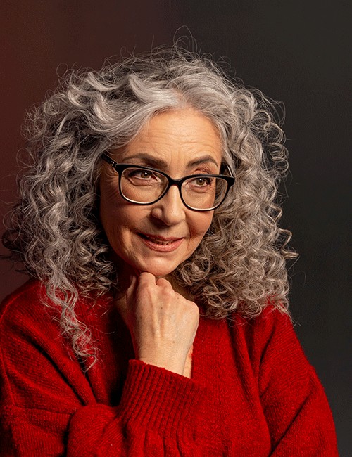 woman over 70 with shoulder-length gray curly hair wearing black glasses