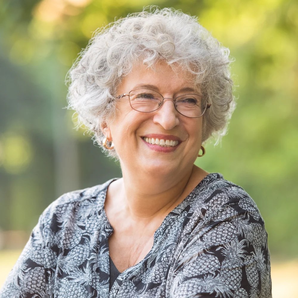 White Curls and Wire Frames in the Garden — short curly haircut on a woman over 70, easy to care for