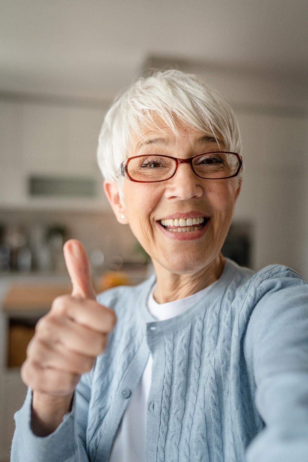 smiling woman over 70 with a neat white pixie cut wearing red glasses