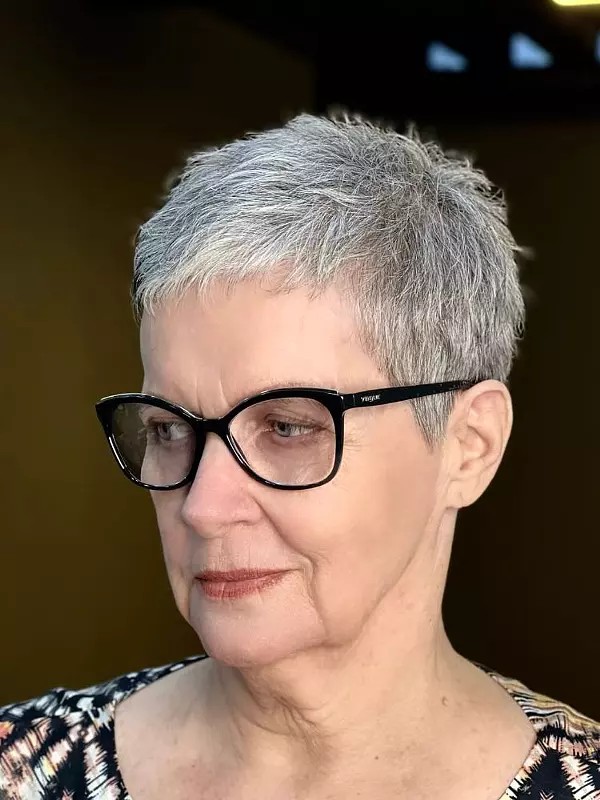 woman over 70 with a steel-gray short crop wearing statement glasses