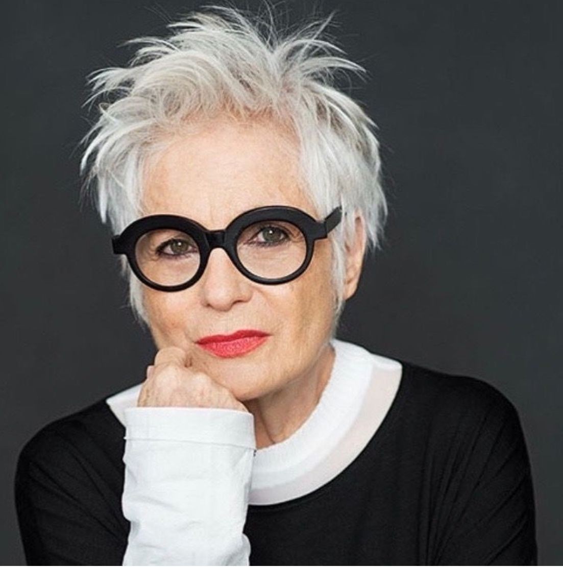 woman over 70 with a spiky white pixie cut wearing round statement glasses