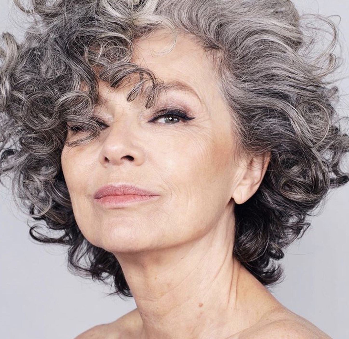 The Volumized Dark-Gray Curly Bob — soft perm curls on a woman over 70 with flat hair